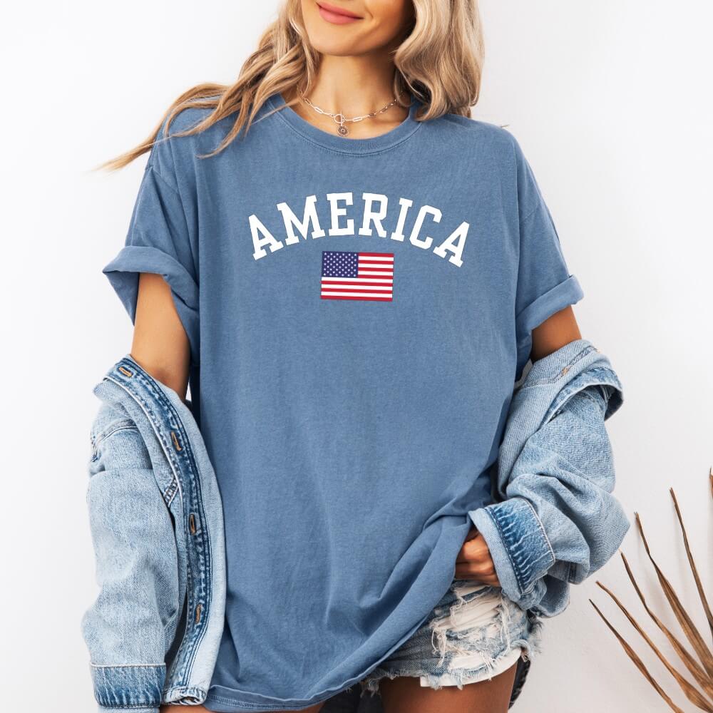 America T-shirt blue jean color. Short sleeve unisex t-shirt with American flag printed on the front, above it is printed "America" in white font.
