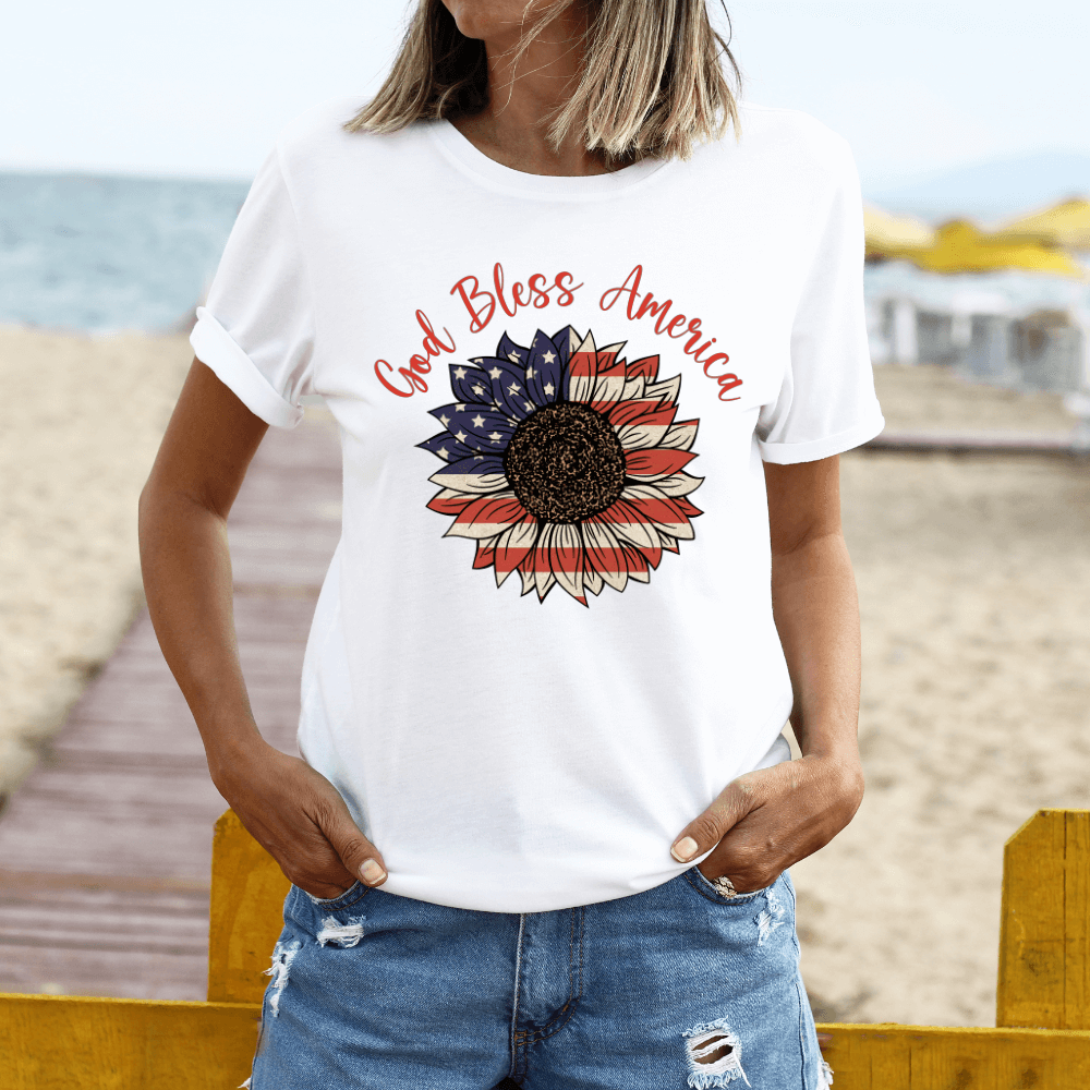 Women's God bless America t-shirt white. Crewneck short sleeve t-shirt with an American Flag colored sunflower on the front chest.