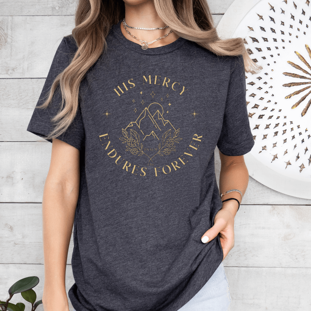 His Mercy Endures forever short sleeve women's t-shirt dark heather grey.  Design of mountains in tan with "His Mercy Endures Forever" printed on the front around the design. "Psalm 136" printed in small font.