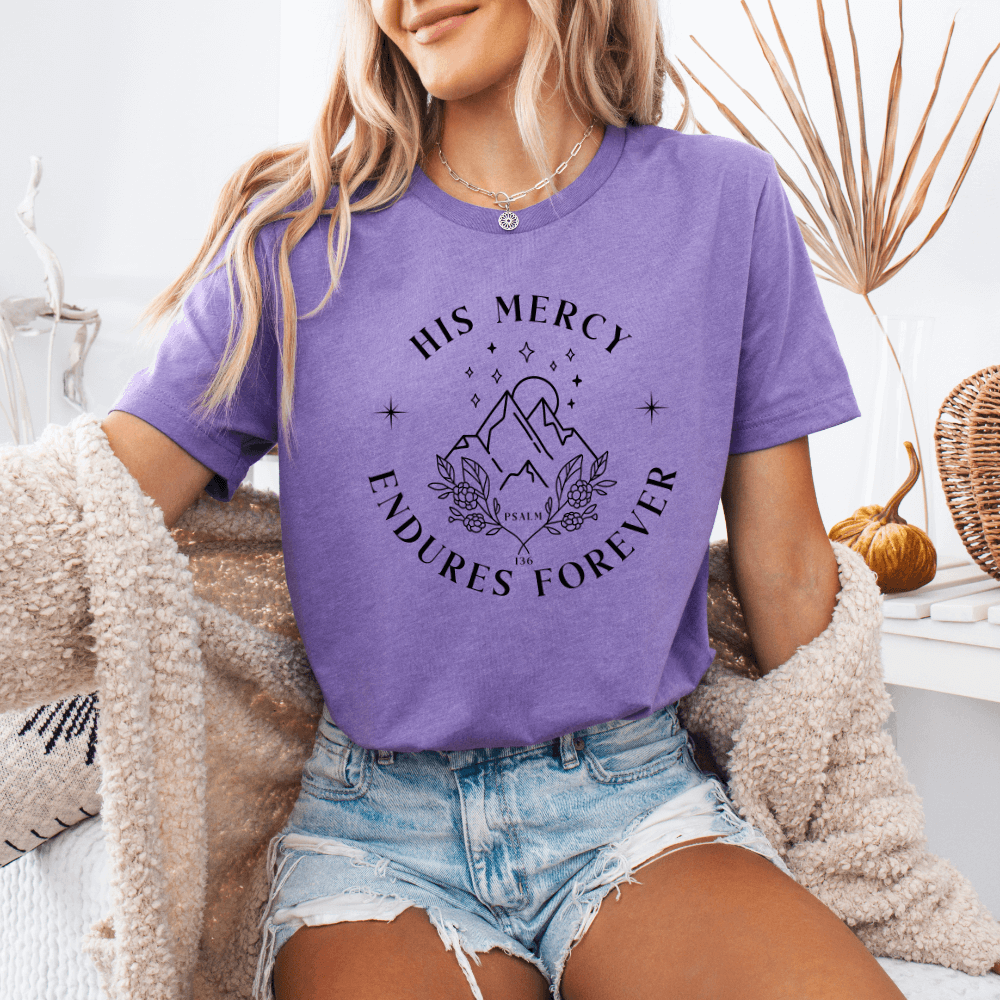 His Mercy Endures forever short sleeve women's t-shirt heather purple.  Design of mountains in black with "His Mercy Endures Forever" printed on the front around the design. "Psalm 136" printed in small font.