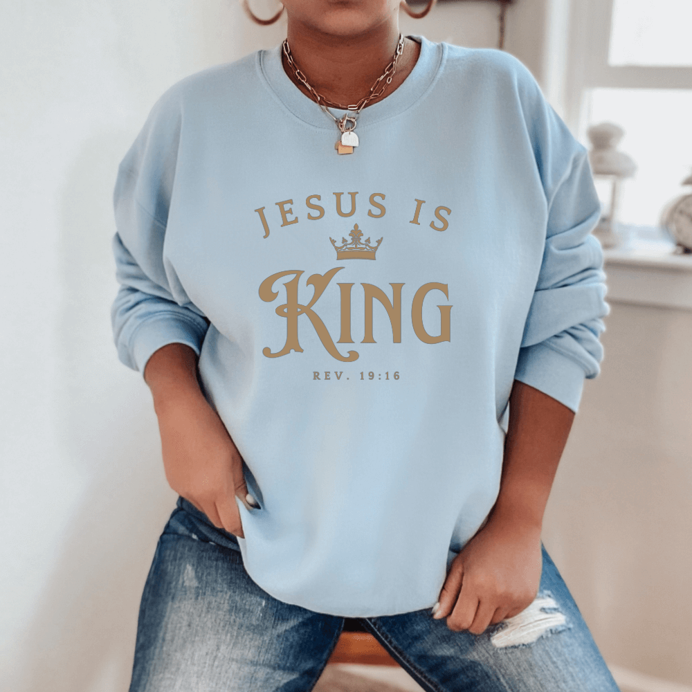 Unisex Jesus Is King Sweatshirt light blue. Design on front  chest in light tan with Rev. 19:16 below the design.