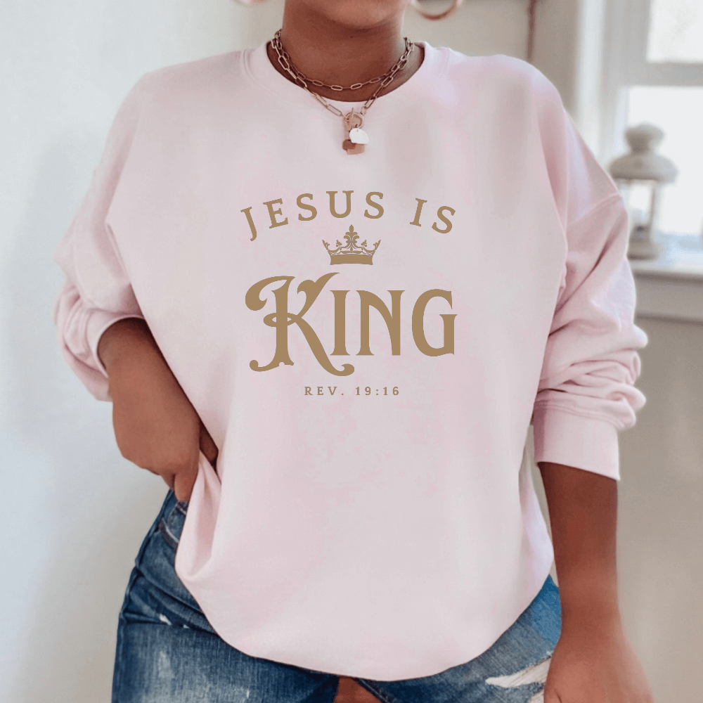 Unisex Jesus Is King Sweatshirt light pink. Design on front  chest in light tan with Rev. 19:16 below the design.
