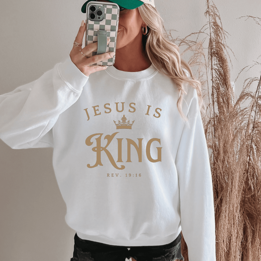 Unisex Jesus Is King Sweatshirt white. Design on front  chest in light tan with Rev. 19:16 below the design.