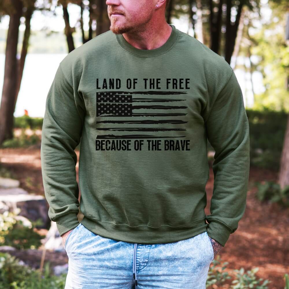Land of the Free Sweatshirt military green. Unisex crewneck sweatshirt with an American flag printed in black on the front chest. "Land of the free Because of the Brave' is written above and below the flag.