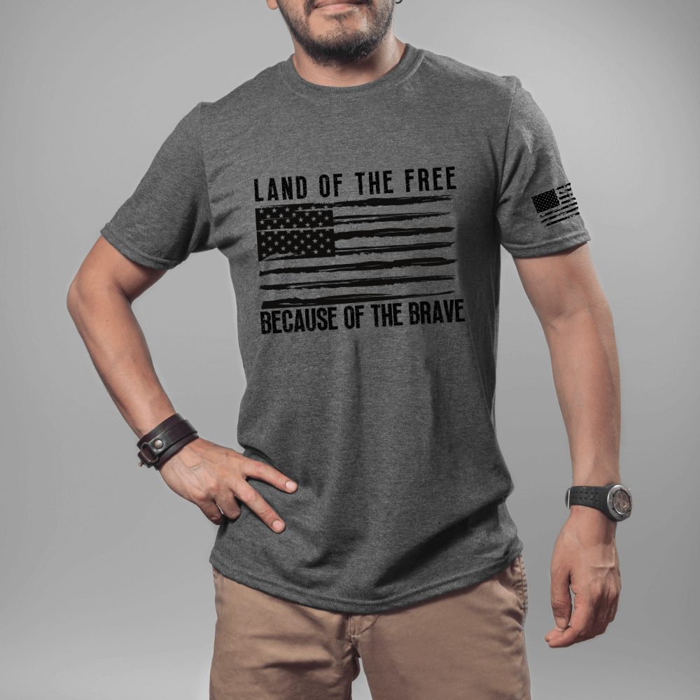 Land of the Free t-shirt, short sleeve dark heather. American flag printed in black on front chest with 'Land of the Free, Because of the Brave" written above and below the flag.  American flag is also printed on the left sleeve.