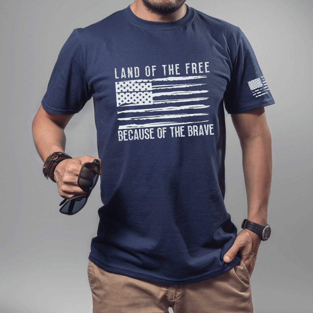 Land of the Free t-shirt, short sleeve navy. American flag printed in white on front chest with 'Land of the Free, Because of the Brave" written above and below the flag.  American flag is also printed on the left sleeve.