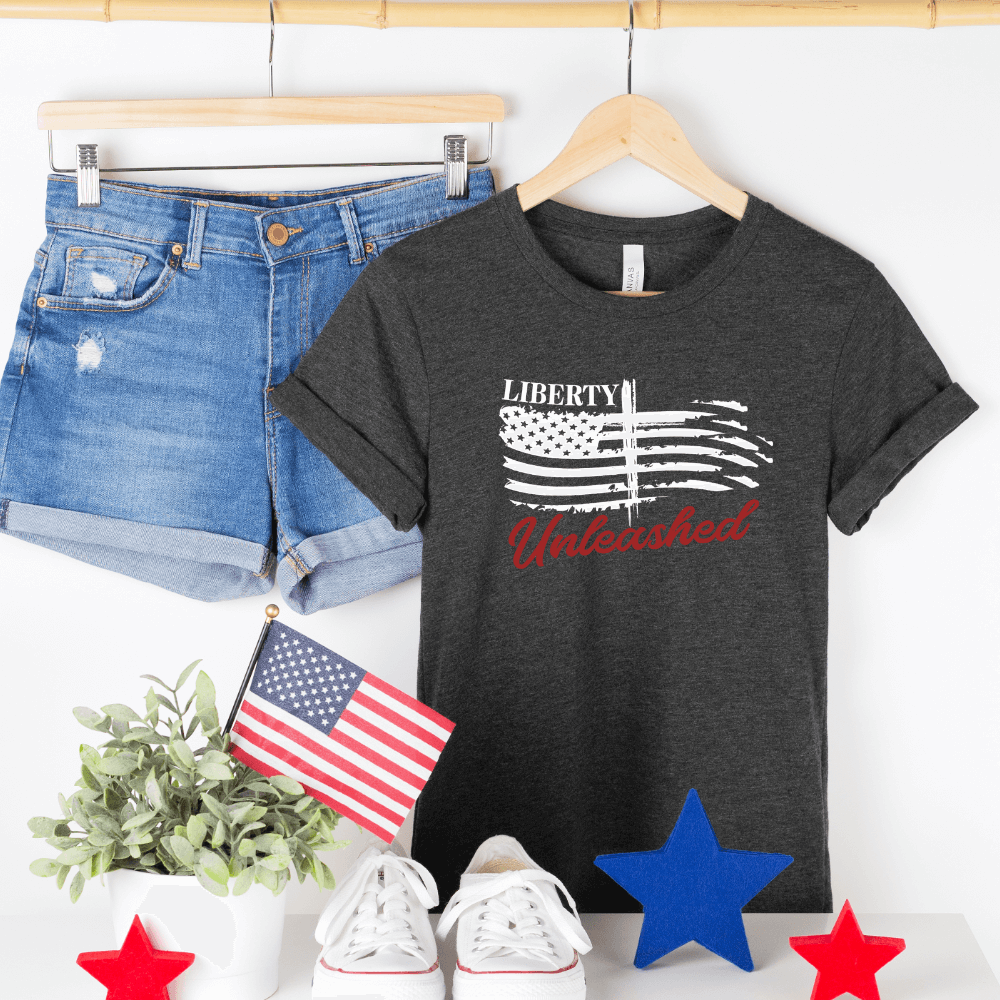 Liberty Unleashed Unisex T-shirt short sleeve dark grey heather.  White American flag on the front chest with a cross in the middle and "Liberty Unleashed" printed above and below the flag.