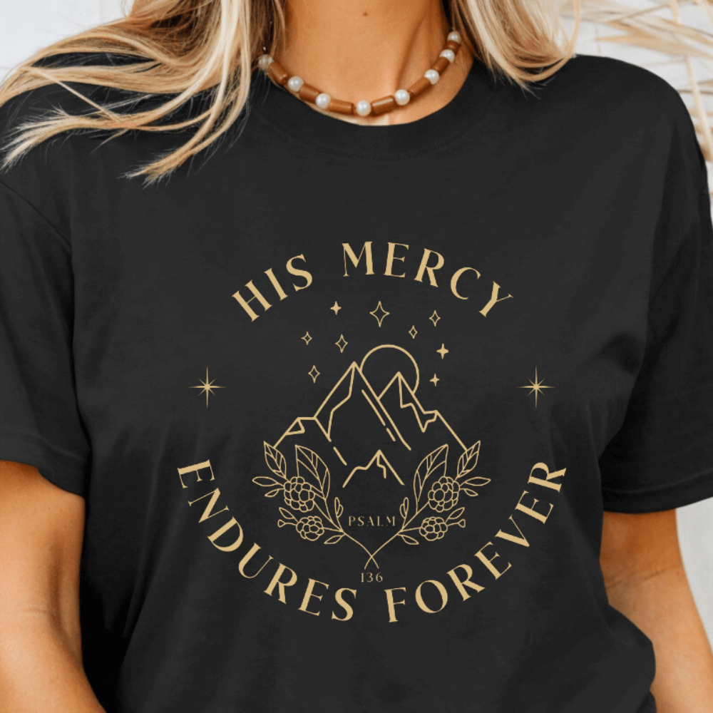 His Mercy Endures forever short sleeve women's t-shirt black.  Design of mountains in tan with "His Mercy Endures Forever" printed on the front around the design. "Psalm 136" printed in small font. 