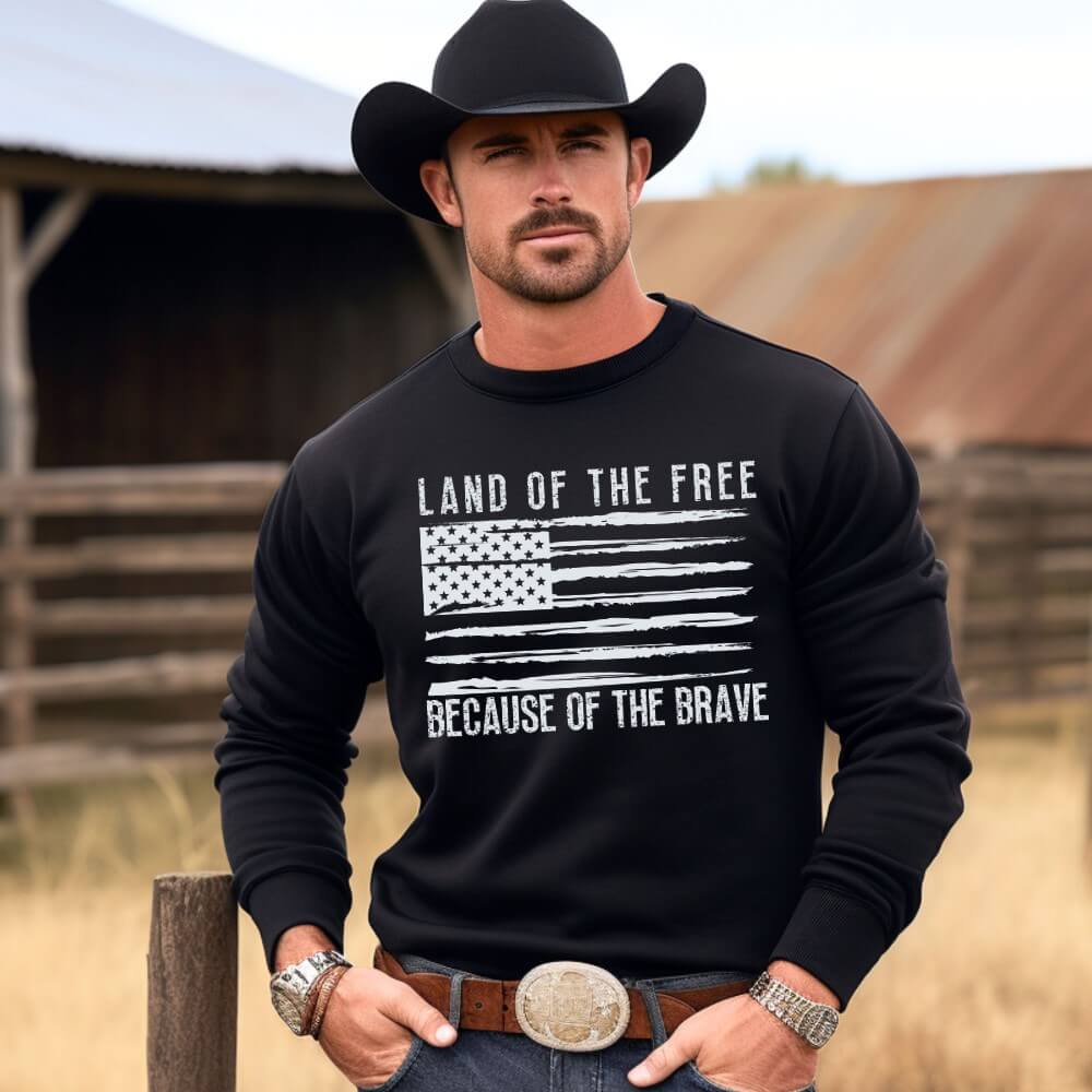 Land of the Free Sweatshirt. Unisex crewneck sweatshirt black with a light an American flag printed in light grey on the front chest. "Land of the free Because of the Brave' is written above and below the flag. 
