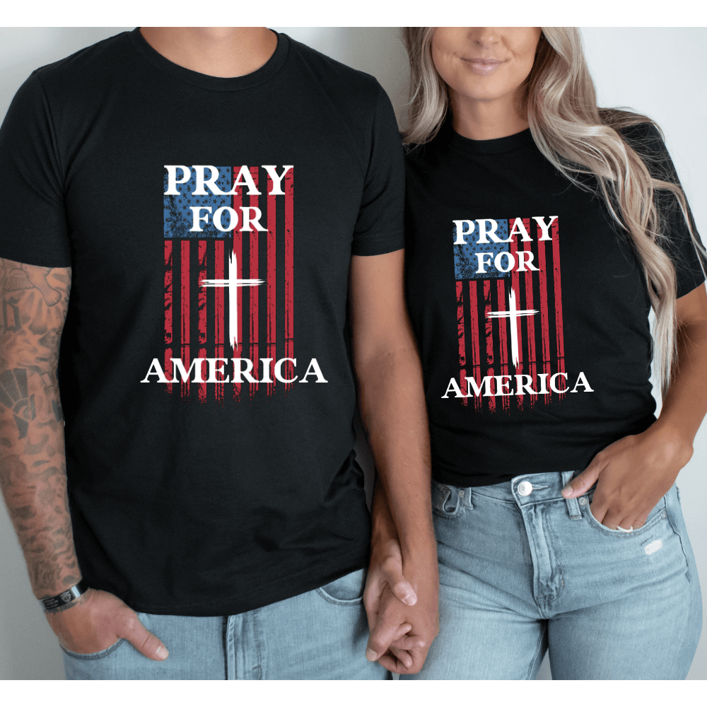 Unisex Pray For America t-shirt short sleeve black.  An American Flag is printed on the front chest with a white cross in the middle and "Pray for America" written above and below the flag. 